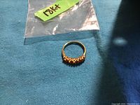 Ring on blue cloth with plastic bag labeled 18K+. Shows overall view of gold band and stones.
