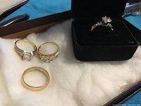 Four rings displayed on white padding with one ring in a black box.