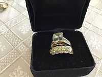 Front view of both rings in black jewelry box showing cushion-cut green stone and row of round green stones