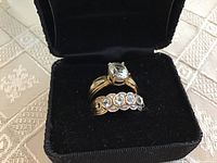 Both rings seated in black velvet ring box on patterned cloth