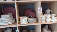 Overview of stacks of plates, bowls, cups, saucers, gravy boat and matching serve pieces arranged on shelf.