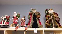 Photo shows eight Santa figurines and ornaments arranged on a shelf, various sizes and materials including ceramic and fabric, in older vintage styles with accessories such as baskets and wreaths.