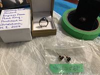 Full view of all items: two rings (one pearl ring in box) and one pair of small stone-studded sterling silver earrings in plastic bag.