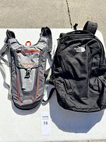 Two backpacks displayed on table: Outdoor Products hydration pack in grey/red, and larger black The North Face Karst backpack.