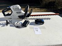 Hedge trimmers with battery and charger laid out on white table.