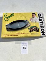 Boxed Emerilware cast iron sizzle plate with trivet, showing front of the box with branding and images.