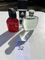 Three men's cologne bottles displayed together: Hero for Man red bottle, Adidas Dynamic Pulse in box, and Realities for Men clear bottle.