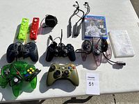 Gaming accessories including various controllers, two Wii remotes with silicone cases, a PS4 game, and a small plastic storage box