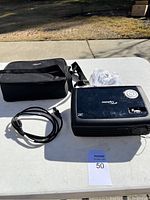 Photo of projector, carrying case, power cable and remote on white table outdoors