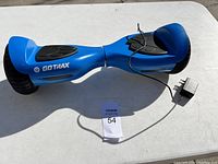 Blue GOTRAX hover board laid on white surface with charger connected and placed beside it