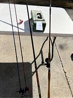 Three fishing rods and one green tackle box displayed on and next to a white table outside.