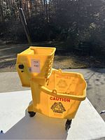 Yellow industrial mop bucket on wheels with metal mop wringer attached, caution signs visible