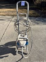 Full view of the industrial paint sprayer unit mounted on a metal cart with handle and coiled hose.