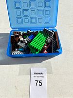 Open blue plastic container showing assorted Lego bricks in multiple colors and sizes including a large green baseplate.