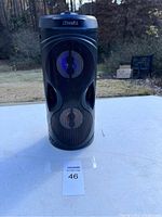Front view of black cylindrical Sylvania Bluetooth speaker with blue LED lights glowing inside the speaker grilles.