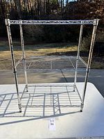 Front view of the metal wire rack shelving unit showing three metal wire shelves, vertical posts, and black plastic feet.