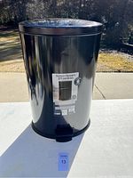 Full view of the black metal oval trash can with pedal, showing the label and exterior.
