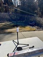 Full view of the black tripod boom microphone stand set up outdoors on a table, showing the stand and the long adjustable boom arm.