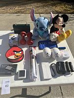 Full overview of miscellaneous items on white table including plush toys, dumbbells, cables, and electronic accessories.