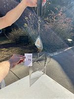 Metal kinetic spinner sculpture with nested square frames and central diamond shape, hung outdoors to show size and reflective surfaces.