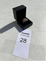 Ring inside black jewelry box, displayed on white surface with auction number 28 card beside it.