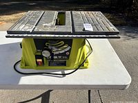 Front angled view showing Ryobi 10-inch table saw with metal work surface and visible blade slot.