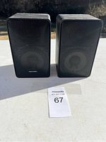 Two black Technics speakers front view on a white surface with a lot number in front.