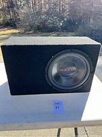 Front view of the Orion subwoofer in its carpeted enclosure showing the speaker cone and logo clearly.