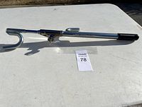 Full view of the chrome metal steering wheel lock with key on white table, showing device shape and lock mechanism.