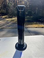 Front view of black tall tower fan showing slim body and circular base on white table outdoors
