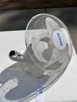White Hurricane wall mounted fan showing the protective mesh grill and five blades with brand name visible.