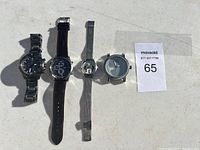 Four wristwatches laid flat: two men's watches, one women's watch, and one watch face only.