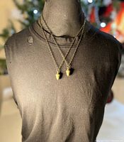 Two brass acorn pendant necklaces worn on a black mannequin torso showing length and overall style