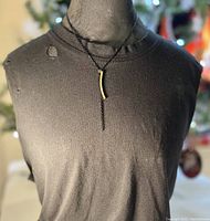 Full view of black metal chain necklace with vertical gold plated curved pendant displayed on black fabric bust.