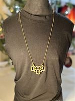 Photo showing the full length of the brass geometric pendant necklace worn over a black top, highlighting chain length and pendant size.