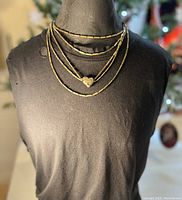Mannequin bust wearing multi-layered vintage brass chain necklace with bronze heart-shaped pendant at center.