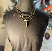 Full view of the necklace on a black display bust showing the layered antique brass chains and bullet pendant.