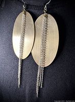 Front view of the hand brushed gold-tone oval earrings with hanging silver and gold plated chains