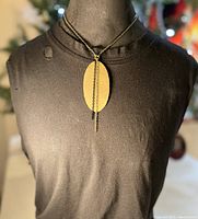Front view of brass oval pendant on black chain necklace displayed on a mannequin.