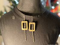 Pair of gold plated rectangular window pendant earrings with chain accents shown on black mannequin bust.