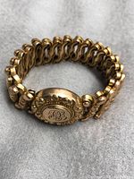 Front view of the vintage gold-tone stretch bracelet showing its detailed central monogram clasp.