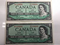 Front view of two 1954 Canadian one dollar bank notes showing crown portrait and serial numbers 21109284 and 21109285.