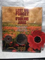 Front of sealed pack showing Lest We Forget title, English and French text, two commemorative coins visible through blister pack with poppy flower background.