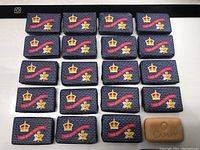 Twenty bars of soap wrapped in commemorative navy blue packaging for the Royal Visit 1959 arranged on a white surface with one unwrapped Camay soap bar.