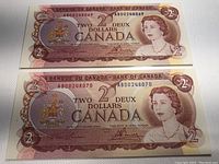 Two 1974 Canadian $2 bank notes shown front side, displaying Queen Elizabeth II portrait, denomination 2 in corners, and Canadian coat of arms, serial numbers AB00248069 and AB00248070.