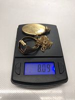 Engraved locket, ring, and chain on digital scale reading 8.09 g