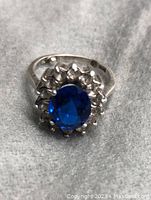 Top-down view of the ring showing the large blue sapphire-colored oval rhinestone surrounded by clear rhinestones in floral design.