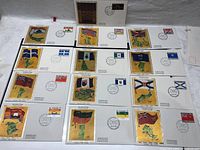 Multiple first day of issue Canadian envelopes featuring different provincial and territorial flags arranged in rows on a white surface.