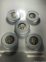 Five silver Mercury dimes in individual clear plastic holders arranged on white surface.