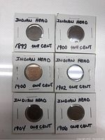 Top view of six Indian Head One Cent coins in holders labeled with years 1893, 1900, 1900, 1902, 1904, and 1906.
